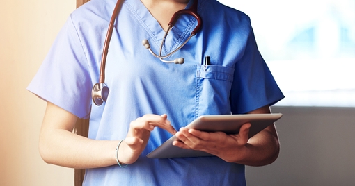A nurse wearing scrubs using a digital tablet