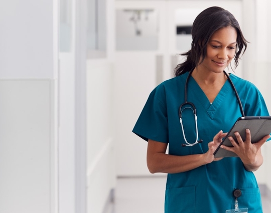 Black woman nurse looking at a tablet with a stethoscope around her neck