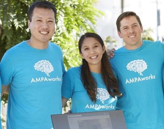 Five people stand and smile for a group photo. They're all wearing light blue t-shirts that say AMPAworks with a brain-shaped graphic.