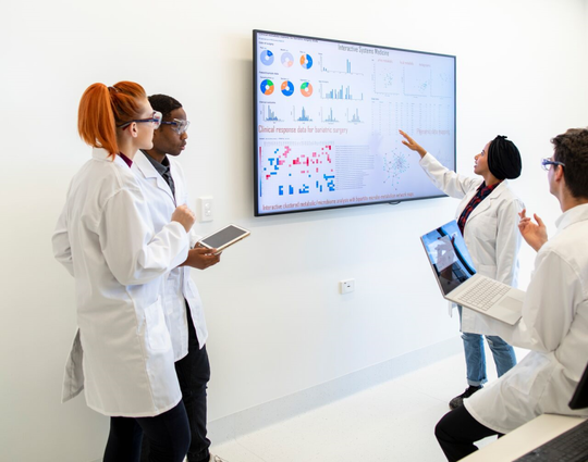 Professional team of medical scientists in a laboratory gathered around a wall monitor